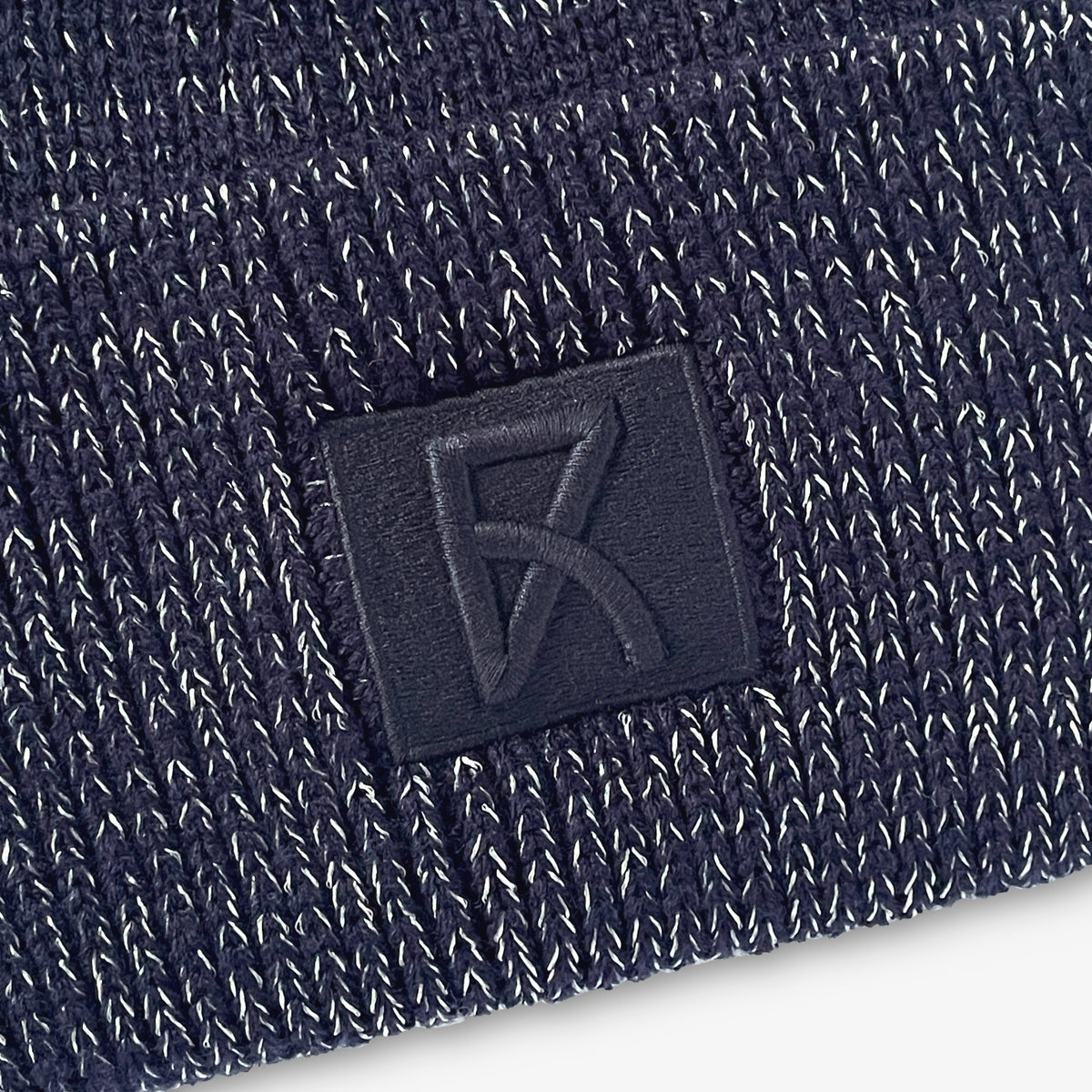 Närbild på den broderade loggan på den marinblå mössan.