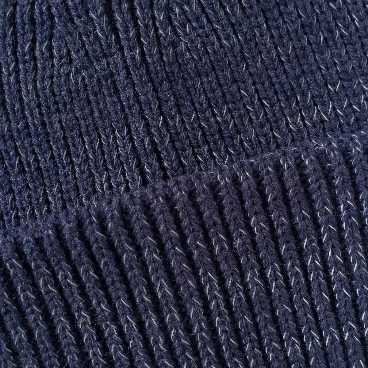 Närbild på garnet på den marinblå mössan.