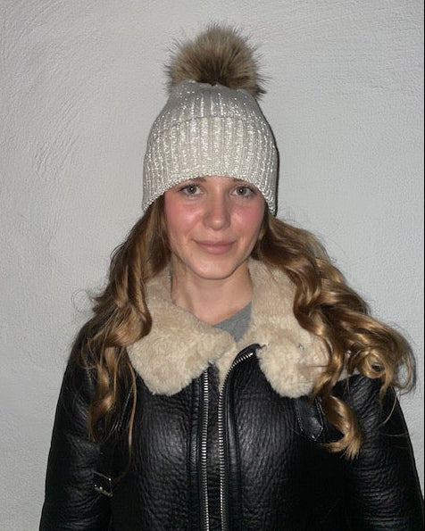 Beige ribbstickad mössa med pälstofs, sedd på modell där reflexen lyser.
