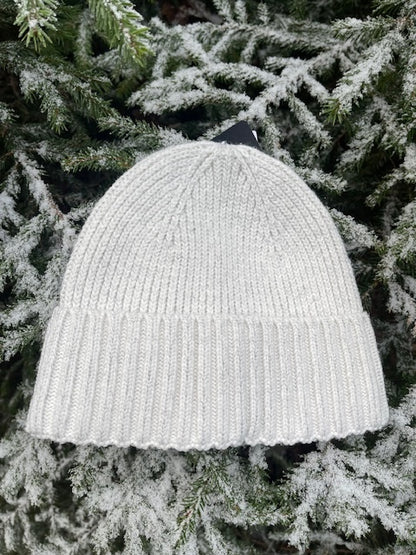 Beige sotarmössa i Polylana®-garn som ligger i granris.