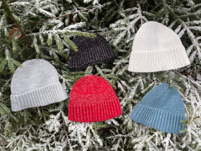 Röd, svart, grå, beige och turkos sotarmössa i Polylana®-garn som ligger i granris.