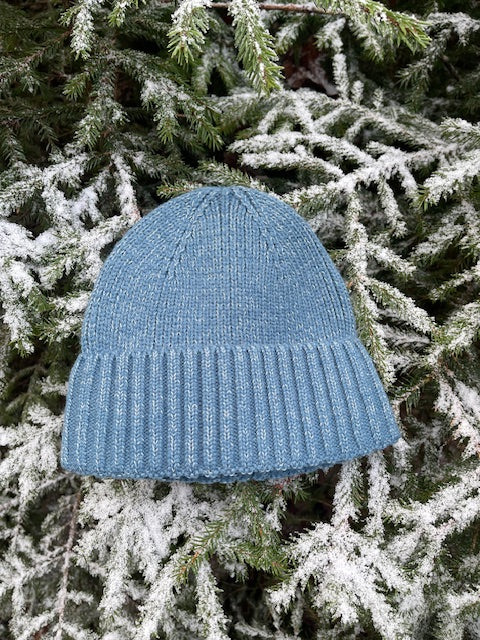 Turkos sotarmössa i Polylana®-garn som ligger i granris.